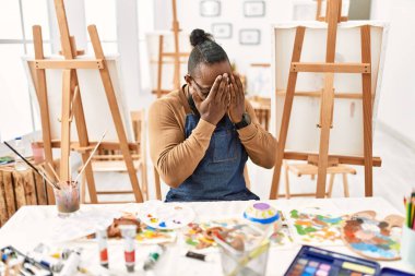 African american artist man at art studio with sad expression covering face with hands while crying. depression concept. 