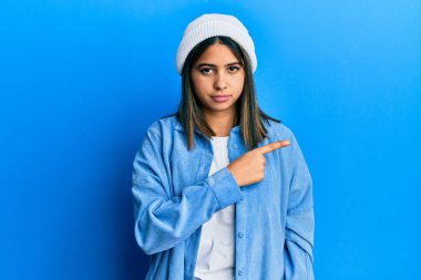 Hoş yün şapkalı genç Latin kadın, el parmağı yanda, ciddi ve sakin bir yüz ifadesi gösteriyor. 