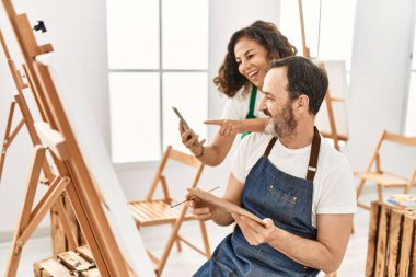 İki orta yaşlı öğrenci resim yaparken gülümsüyor ve resim stüdyosunda akıllı telefon kullanıyor..