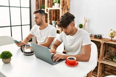 Evde akıllı telefon ve dizüstü bilgisayar kullanan iki İspanyol erkek.