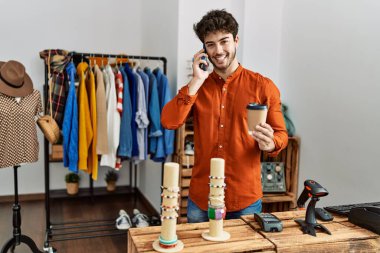 Genç İspanyol esnaf akıllı telefondan konuşuyor ve giyim mağazasında kahve içiyor..