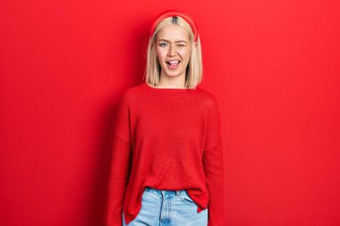 Güzel, kırmızı süveter giyen, seksi bir ifadeyle kameraya bakan, neşeli ve mutlu yüzlü sarışın bir kadın.. 