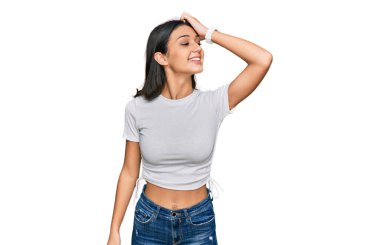 Latin asıllı genç bir kız, günlük beyaz tişört giyiyor, gülümsüyor, saçlarına dokunuyor, el hareketi yapıyor, çekici ve şık bir poz veriyor. 