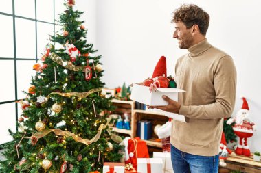Genç İspanyol adam gülümsüyor. Evde kendine güvenen bir Noel ağacı süslüyordu.