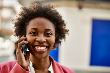 Güzel iş kadını afro saçlı Afro-Amerikan kadın mutlu ve kendinden emin bir şekilde şehirde telefonda konuşuyor.