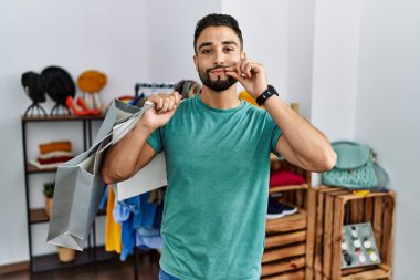 Dükkanda sakallı, alışveriş torbaları tutan genç yakışıklı bir adam. Ağzı ve dudakları parmaklarıyla kapanmış. gizli ve sessiz, tabu konuşması 