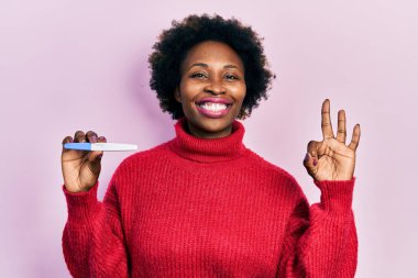 Genç Afrikalı Amerikalı kadın termometreyi tutuyor. Parmaklarıyla imza atıyor, gülümsüyor. Mükemmel bir sembol. 