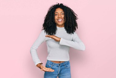 Genç Afro-Amerikan kızı, günlük kıyafetler giymiş, elleri büyük ve büyük beden işareti olan, ölçü sembolü gösteren hareketler yapıyor. Kameraya bakıp gülümsüyor. ölçüm kavramı. 