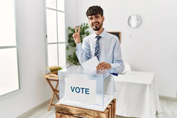 有胡子的西班牙裔人投票把信封放进投票箱 笑容满面 用手指眨眼看着相机做胜利的标志 第二点 — 图库照片