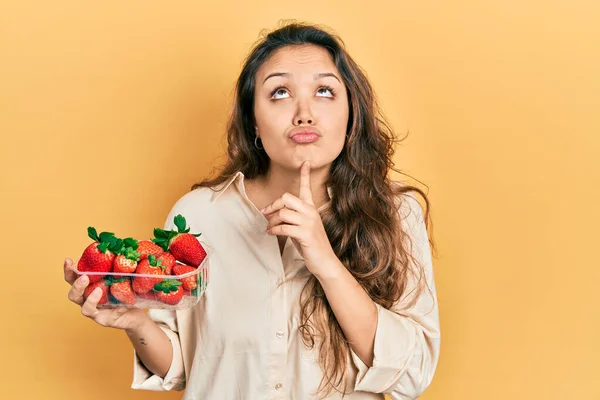 Young Hispanic Girl Holding Strawberries Thinking Concentrated Doubt Finger Chin — 图库照片
