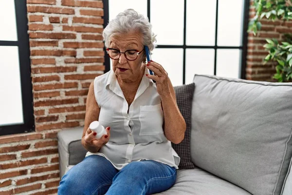 シニア白髪の女性の話上のスマートフォン保持薬で自宅 — ストック写真