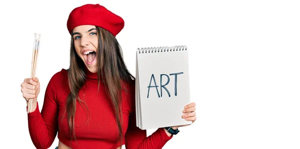 Young Brunette Teenager Holding Art Notebook Paintbrushes Celebrating Crazy Amazed — Stock Photo, Image