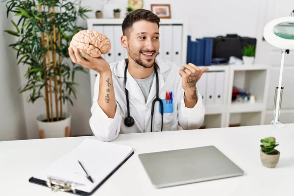 Young Doctor Holding Brain Medical Clinic Pointing Thumb Side Smiling — Foto de Stock