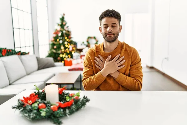 Arab Young Man Sitting Table Christmas Tree Smiling Hands Chest — стокове фото