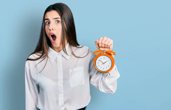 Young Brunette Teenager Holding Alarm Clock Scared Amazed Open Mouth — Stockfoto