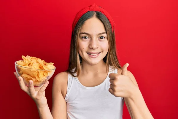 Piękna Brunetka Dziewczynka Trzyma Chipsy Ziemniaczane Uśmiechnięty Szczęśliwy Pozytywny Kciuk — Zdjęcie stockowe