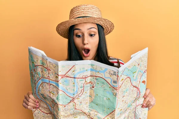 夏の帽子をかぶった若いヒスパニック系の女性が地図を持って恐れていると驚きと驚きの表情でショックを受けました 恐怖と興奮した顔 — ストック写真