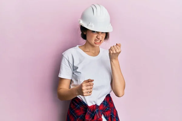 Young Caucasian Woman Wearing Hardhat Angry Mad Raising Fist Frustrated — стоковое фото