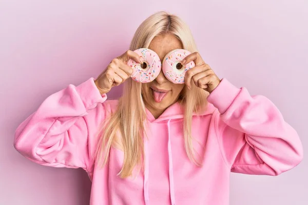 Jovem Mulher Loira Segurando Saborosos Donuts Cor Rosa Sobre Olhos — Fotografia de Stock