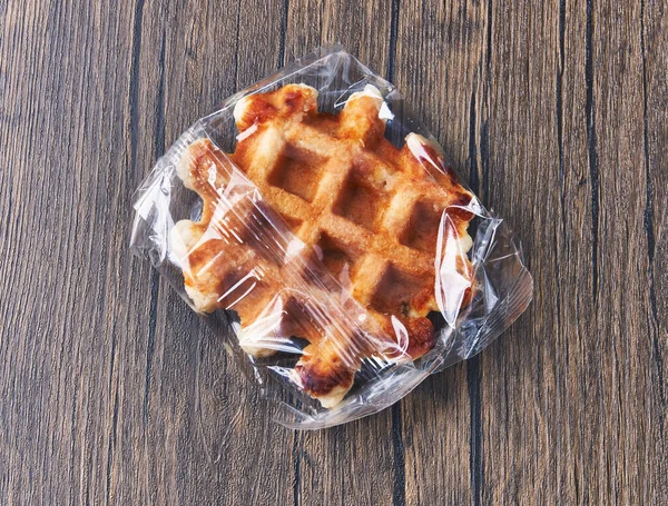 Single Delicious Waffle Wrapped Plastic Bag Wooden Surface — Stockfoto
