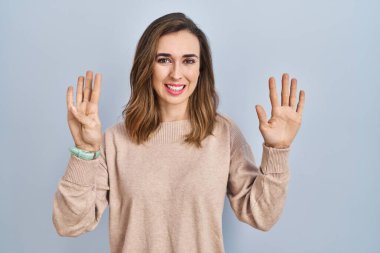 Young woman standing over isolated background showing and pointing up with fingers number nine while smiling confident and happy. 