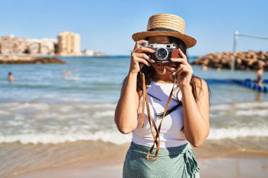 Deniz kenarında kamerayla gülümseyen genç İspanyol kadın.