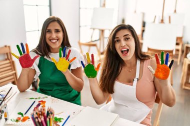 İki Latin öğrenci mutlu bir şekilde gülümsüyor. Sanat okulunda boyalı eller gösteriyorlar..