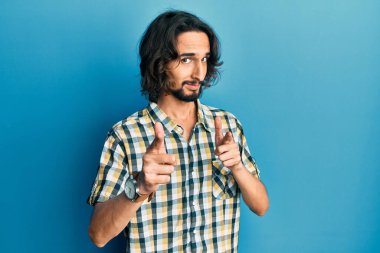 Günlük kıyafetler giyen genç İspanyol adam mutlu ve komik yüzüyle kamerayı işaret ediyor. iyi enerji ve titreşimler. 