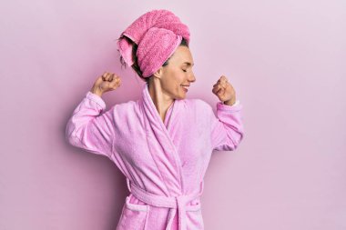 Young blonde woman wearing shower towel cap and bathrobe stretching back, tired and relaxed, sleepy and yawning for early morning 