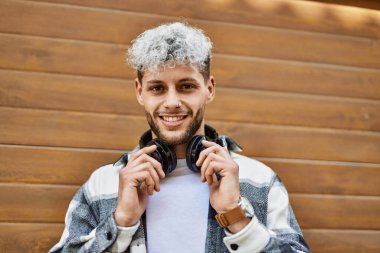 Şehirde kulaklık takarak mutlu gülümseyen genç İspanyol adam..