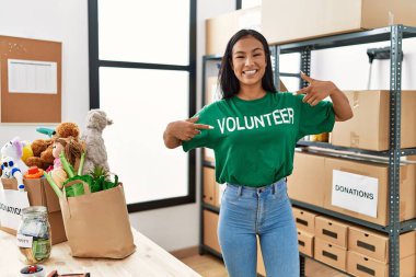 Yardım merkezinde gönüllü üniforma için parmaklarıyla işaret eden genç Latin kadın.