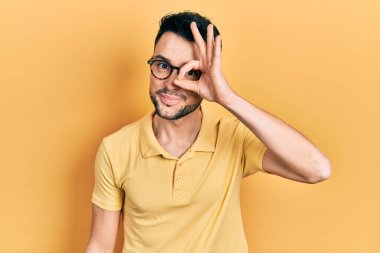 Gündelik kıyafetler ve gözlük takan genç İspanyol adam el hareketleriyle gülümsüyor ve mutlu yüzüyle parmaklarının arasından bakıyor.. 