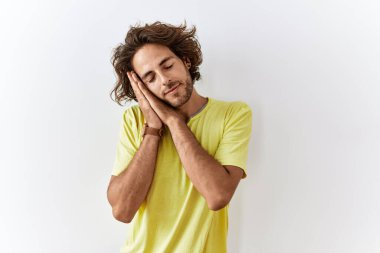 Young hispanic man standing over isolated background sleeping tired dreaming and posing with hands together while smiling with closed eyes. 