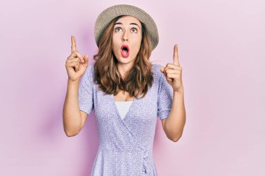 Yaz şapkası takan genç İspanyol kız şaşırdı ve şaşırdı. Yukarı baktı ve parmaklarıyla işaret etti ve kollarını kaldırdı.. 