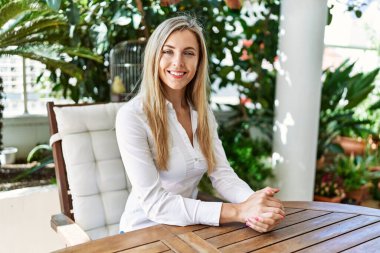 Young blonde woman smiling happy sitting on the table at the terrace.