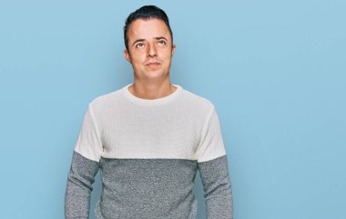 Handsome young man wearing casual winter sweater smiling looking to the side and staring away thinking. 