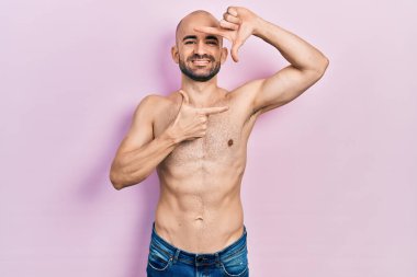 Young bald man standing shirtless smiling making frame with hands and fingers with happy face. creativity and photography concept. 