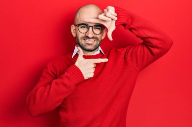 Young bald man wearing casual clothes and glasses smiling making frame with hands and fingers with happy face. creativity and photography concept. 