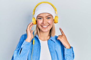 Güzel sarışın kadın müzik dinliyor kulaklık takıyor mutlu bir şekilde el ve parmak işareti yapıyor. 