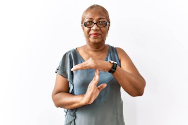 Mature hispanic woman wearing glasses standing over isolated background doing time out gesture with hands, frustrated and serious face 