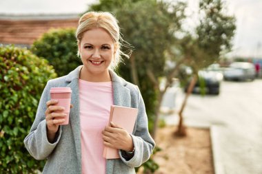 Genç sarışın iş kadını gülümseyerek şehirde kahve içiyor..