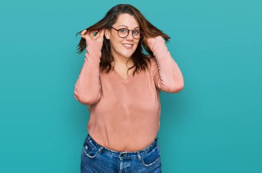 Young plus size woman wearing casual clothes and glasses smiling pulling ears with fingers, funny gesture. audition problem 