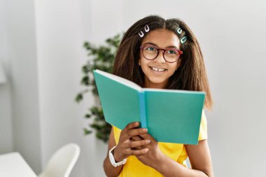 Afro-Amerikalı kız gülümseyerek evde kendinden emin bir şekilde kitap okuyor.