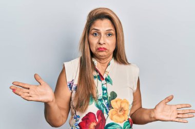 Orta yaşlı İspanyol kadın gündelik kıyafetler giyiyor, elleri ve kolları havada, kafası karışmış bir ifade takınıyor. şüphe kavramı. 