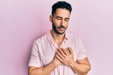 Gündelik kıyafetler giyen genç İspanyol adam elleri göğsünde, gözleri kapalı ve yüzünde minnet dolu bir jest ile gülümsüyor. sağlık kavramı. 