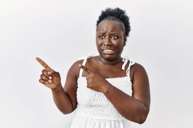 Young african woman standing over white isolated background pointing aside worried and nervous with both hands, concerned and surprised expression 