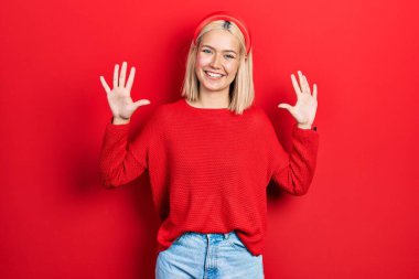 Güzel sarışın kadın gündelik kırmızı süveter giyer ve parmaklarıyla onu gösterirken kendinden emin ve mutlu bir şekilde gülümserdi.. 