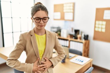 Young brunette teenager wearing business style at office with hand on stomach because indigestion, painful illness feeling unwell. ache concept. 