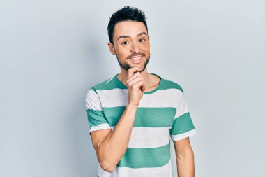 Gündelik kıyafetler giyen genç İspanyol adam kameraya kendinden emin bakıyor kollarını kavuşturup gülümsüyor ve çenesini kaldırıyor. Olumlu düşünmek. 