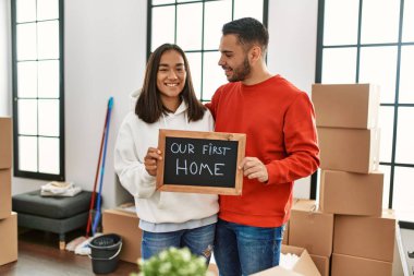 Genç Latin çift mutlu bir şekilde gülümsüyor. İlk ev mesajımızla birlikte ellerinde tahtayla..